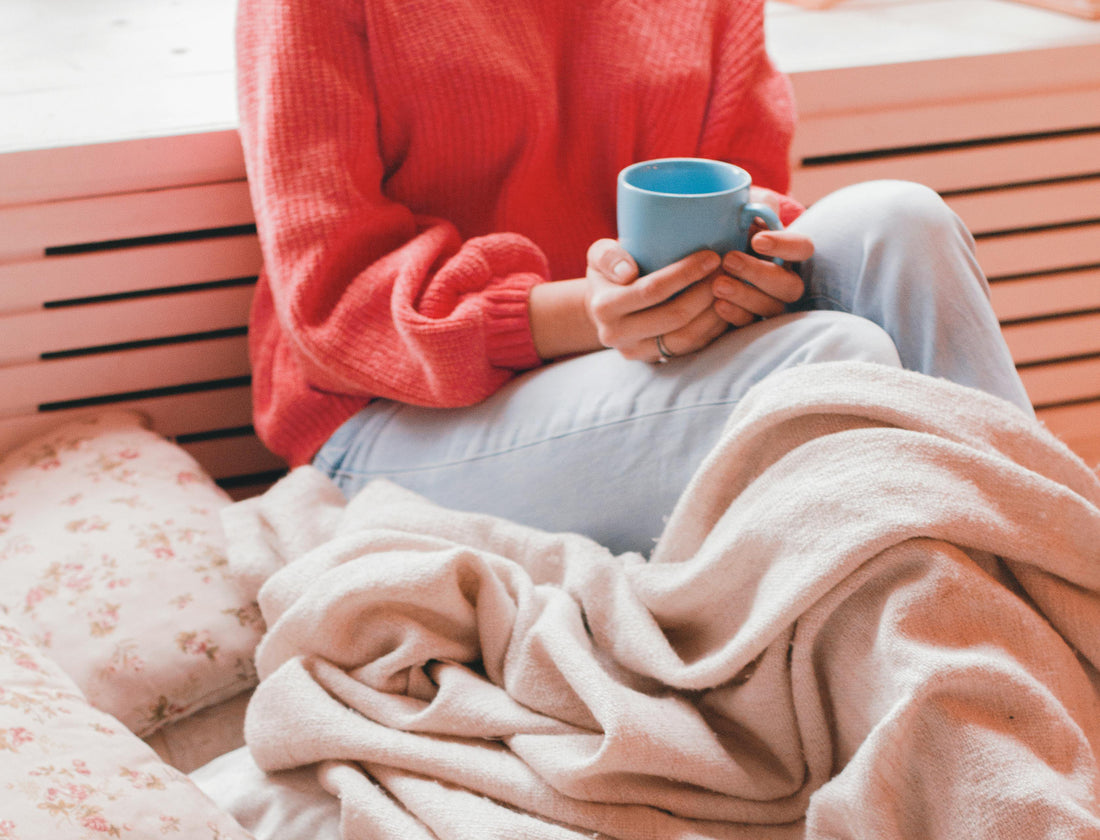 Woman Sitting on Pillows and Under a Blanket Holding a Mug